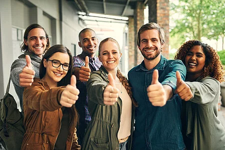 Portrait of a group of happy young students giving thumbs up together on campus