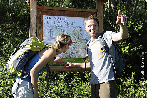 Zwei Wanderer stehen vor einer Tafel vom Wanderweg - Der Natur auf der Spur –