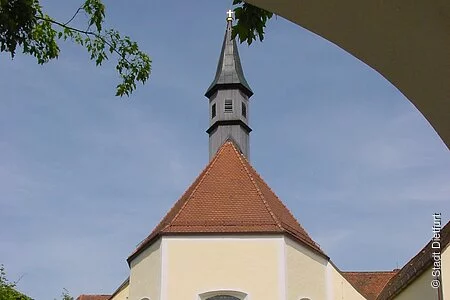 Blich durch den Torbogen auf die Franziskanerkirche mit geöffneter Kirchentür und dem Kirchenvorplatz im Vordergrund.