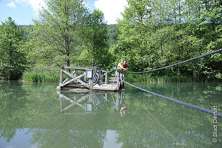 Mit eigener Kraft ziehen Radfahrer auf dem Holzfloß über den Alten Kanal bei Dietfurt.