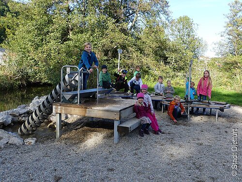 Archimedische Schraube mit Matschtisch am Spielplatz beim Franziskuspark mit spielenden Kindern.