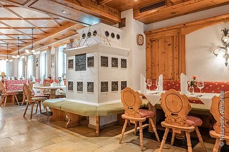 Traditionell bayerische Gaststube der Krone in Kinding. Eingerichtet mit einem typisch bayerischen gemauerten Kamin und Sitzmöglichkeiten drum herum sowie viele Holzelemente (Holzdecke, Teilvertäfelung an den Wänden, Holzstühle).