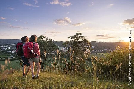 Zwei Frauen mit Wanderrucksäcken stehen am Frauenberg und genießen den Sonnenuntergang, sowie den schönen Blick über Eichstätt.
