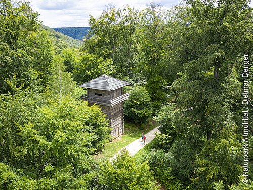 Wanderer unterwegs auf dem Altmühltal-Panoramaweg sind gerade auf Höhe des Limesturms in Kipfenberg. Dieser steht inmitten grüner Bäume.