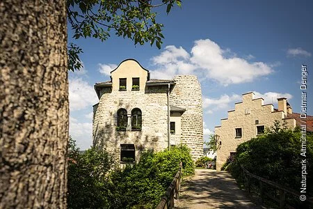 Die Burgruine Altmannstein ist über eine Fußgängerbrücke erreichbar. Links und rechts sind Gebäude, die als Wohnhaus genutzt werden und im Hintergrund ragt der Hungerturm empor. Vom ehemaligen Wohnbau sind nur noch Reste vorhanden.