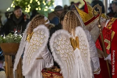 Zwei Mädchen mit Engels- und Mann im Nikolauskostüm beim Gabenverteilen