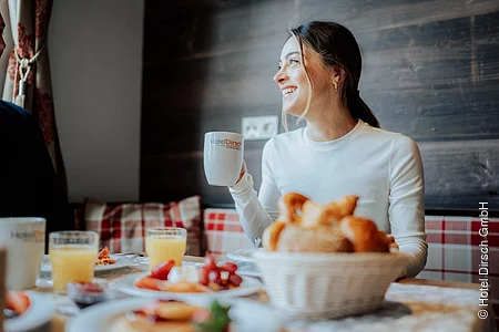 eine Frau sitzt an einem Tisch, der reichlich mit Angeboten vom Frühstücksbuffet gefüllt ist.