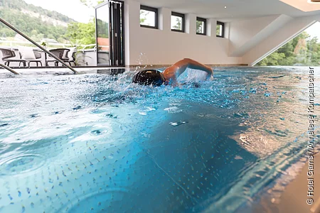 Ein Schwimmer zieht seine Bahnen im Becken. Im Hintergrund sind die Fenster mit dem Panoramablick zu sehen.