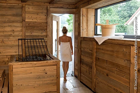 Eine Dame verlässt im Hintergrund das Spahaus aus Holzverkleidet mit einem Saunaangebot des Hotels