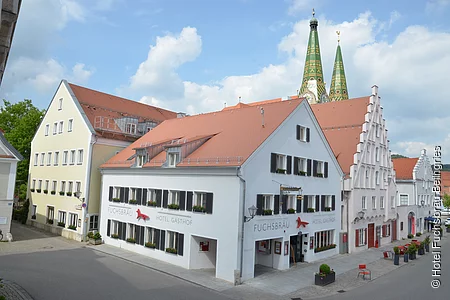 Das Hotel an der Ecke ist weichgestrichen mit grünen Fensterläden. Im Hintergrund sind grüne Kirchtürme zu erkennen.