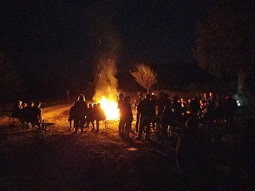 Menschen sitzen im Dunkeln um ein Lagerfeuer herum.