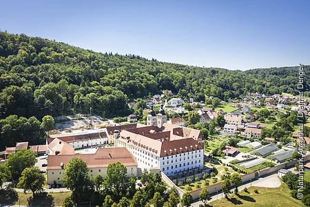 Das Kloster Plankstetten von oben. Der Gebäudekomplex ist umgeben von Bäumen und grünen Wiesen. Vereinzelt sind rechts Häuser zu erkennen.