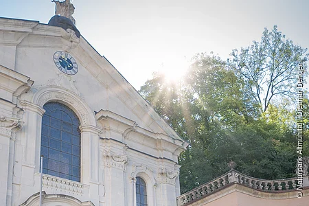 Zwei Frauen und ein Mann stehen vor der Kirche im Klosterinnenhof und bestaunen das Gebäude von außen.