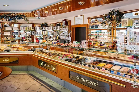 Die Theke mit Vielzahl an Produkten wie Kuchen/Torten/Pralinen und Gebäck dargestellt in dem dekorierten Eingangsraum