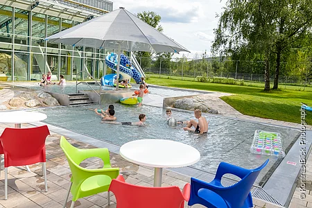 Außenbereich des Sport- und Freizeitbades Greding mit Planschbecken, Wasserrutsche und Sitzgelegenheiten