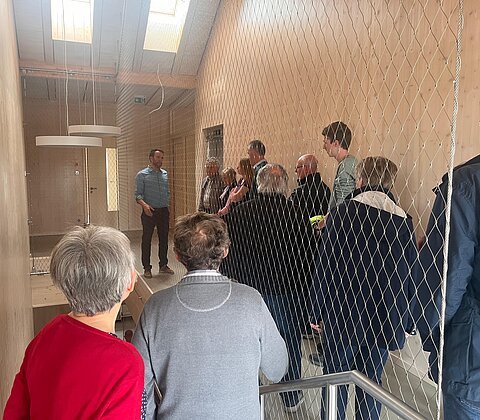 Viele Menschen stehen im Flur/Treppenhaus. Architekt erklärt Bauweise.