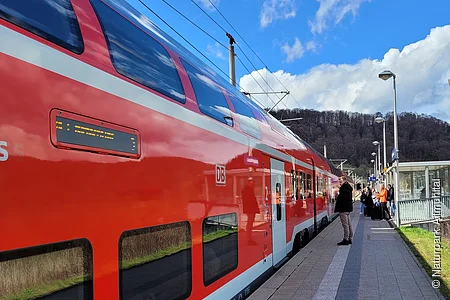Eine Regionalbahn hat am Gleis gehalten und Reisende warten darauf, dass sich die Türen öffnen.