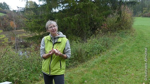 Am Rand eines Baches erklärt steht die Naturparkführerin und erklärt den Teilnehmern