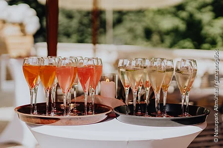 Auf einem weißen Partystechtisch befinden sich zwei braune Tabletts. Auf einem Tablet stehen Weinbläser mit weißem Sekt und auf dem anderen Weingläser mit rose farbenem Sekt.