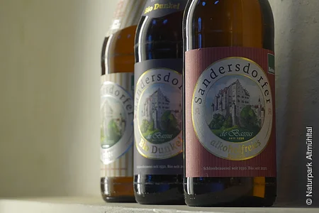 Drei Bierflaschen der Marke Sandersdorfer auf einem Regal mit Etiketten mit Schlossabbildung.