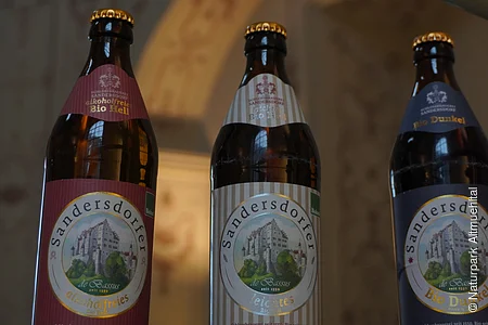 Drei Bierflaschen mit Etiketten der Marke Sandersdorfer, Sorten: alkoholfrei, leichtes, dunkel.