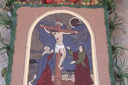 Der Körnerteppich zeigt Jesus am Kreuz mit seiner Mutter Maria und dem Jünger Johannes.