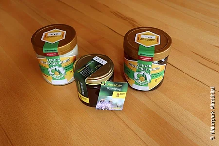 Drei Honiggläser mit Etiketten "Echter Deutscher Honig" auf einem Holztisch.