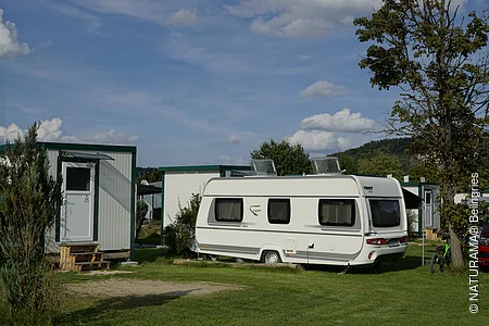 Wohnwagen auf einem Campingplatz neben kleinen Gebäuden und einem Baum.