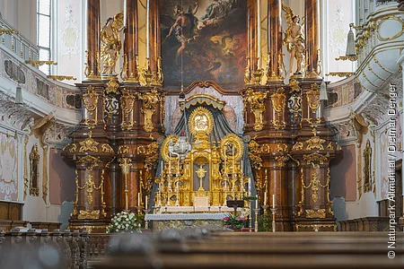 Barocker Kirchenaltar mit reich verzierten goldenen Elementen und Gemälde im Hintergrund.