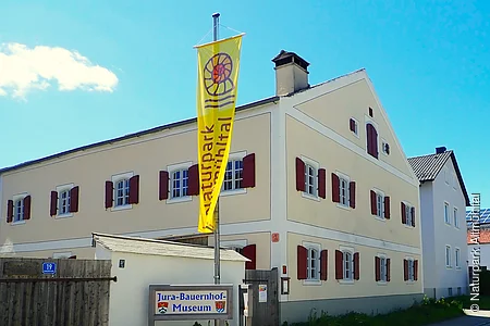 Gebäude mit gelber Flagge "Naturpark Altmühltal" und Schild "Jura-Bauernhof-Museum" davor.