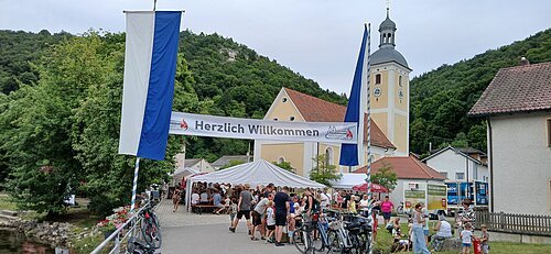 Quellenfest Mühlbach Das Foto zeigt die Gäste des Quellenfestes an Bierbänken sitzend in der malerischen Mitte von Mühlbach.
