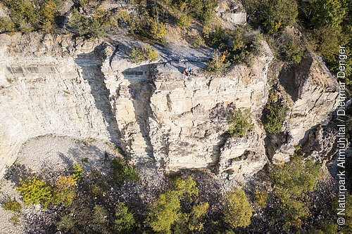 Felsklippe mit Bäumen und Personen auf dem Plateau, aus der Vogelperspektive.