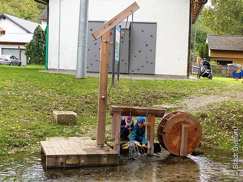 Mühlrad mit Schwengelpumpe Mühlrad aus Holz mit Schwengelpumpe am Mühlbach und zwei spielende Kinder