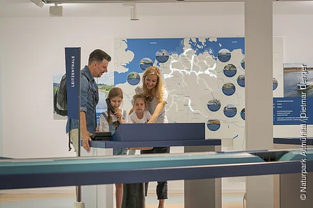 Familie mit zwei Kindern steht an interaktivem Ausstellungstisch vor beleuchteter Deutschlandkarte im Museum.