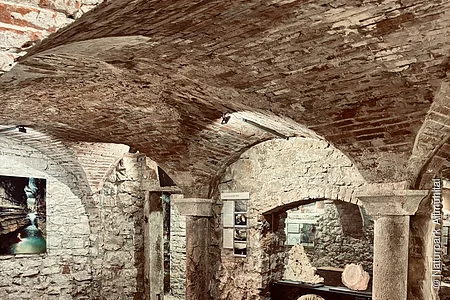 ein gemauertes Gewölbe mit einigen Exponaten zwischen den Bögen. Schummeriges Licht