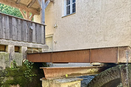 Das Wasserrad wird von einer Rinne angetrieben. Links hinten ist ein hölzerner Wehrgang zu sehen.