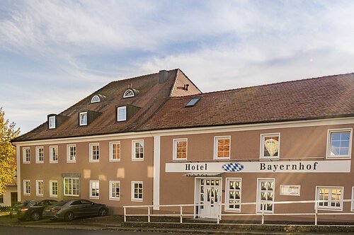 Fassade des Hotels Bayernnhof mit braunem Dach und mehreren geparkten Autos davor bei Tageslicht.