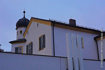 Gebäude mit weißer Fassade, grünen Fensterläden und einem Turm mit schwarzer Kuppel bei Dämmerung.