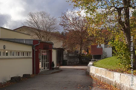 Außenansicht eines Gebäudes mit Bäumen und Gehweg im Herbst bei bewölktem Himmel.