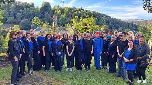 Gruppenfoto von 30 Personen im Freien vor bewaldeten Hügeln bei Tageslicht.