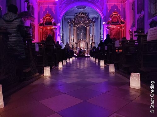 Adventsandacht in der Jakobuskirche Innenraum einer Kirche mit beleuchteten Papierlaternen entlang des Mittelgangs und Menschen auf den Bänken, violett beleuchtet