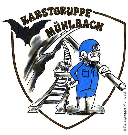 Zeichnung in Wappenform, darauf Höhlenforscher mit Pickel vor Gleisanlage, darüber Schriftzug "Karstgruppe Mühlbach"
