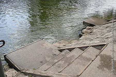 Betonstufen mit Holzgeländer führen von einem Ufer zum Wasser eines Flusses oder Sees.