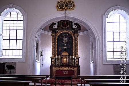 Innenraum einer Kirche mit Altar, zwei großen Fenstern und Holzbänken auf beiden Seiten