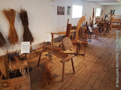 Historische Flachsbearbeitungsgeräte und gebündelte Flachspflanzen in einem Museum mit Holzboden.