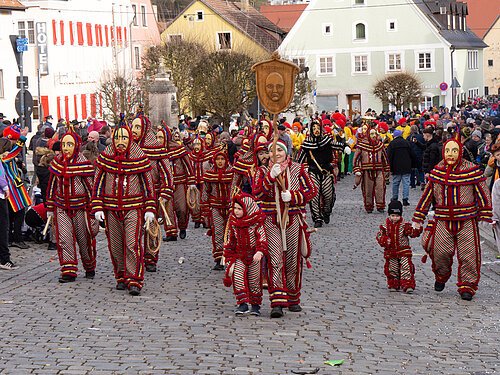 Faschingsumzug in Greding Menschen in gestreiften Kostümen und Holzmasken bei Umzug auf gepflasterter Straße vor Zuschauern